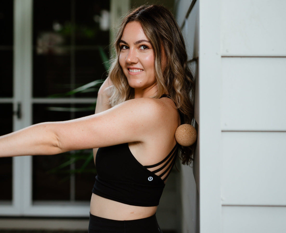Yogi standing against a wall using a cork massage ball on her upper back