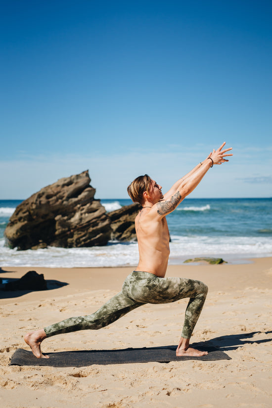 Man practicing yoga on a beach with ocean and sky in the background